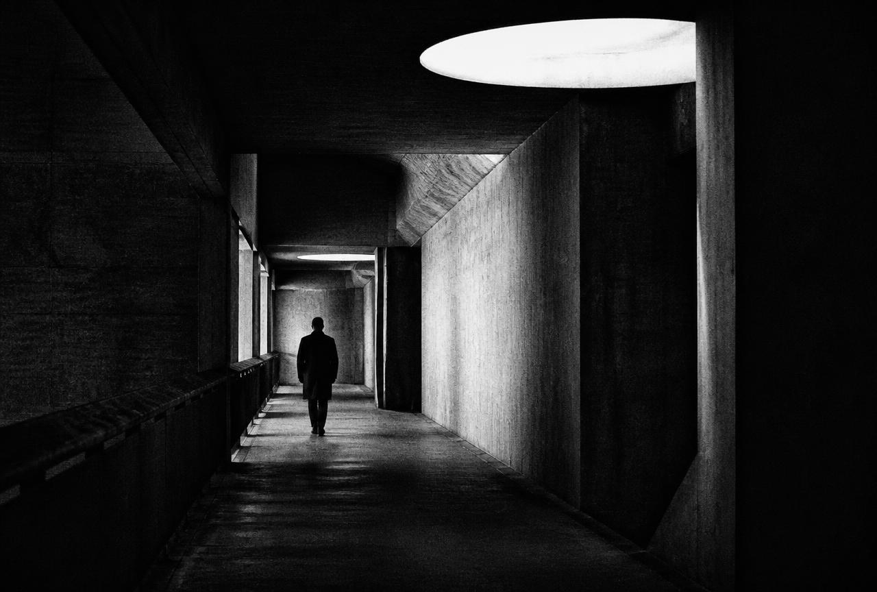 Lone figure walking through a stark concrete corridor